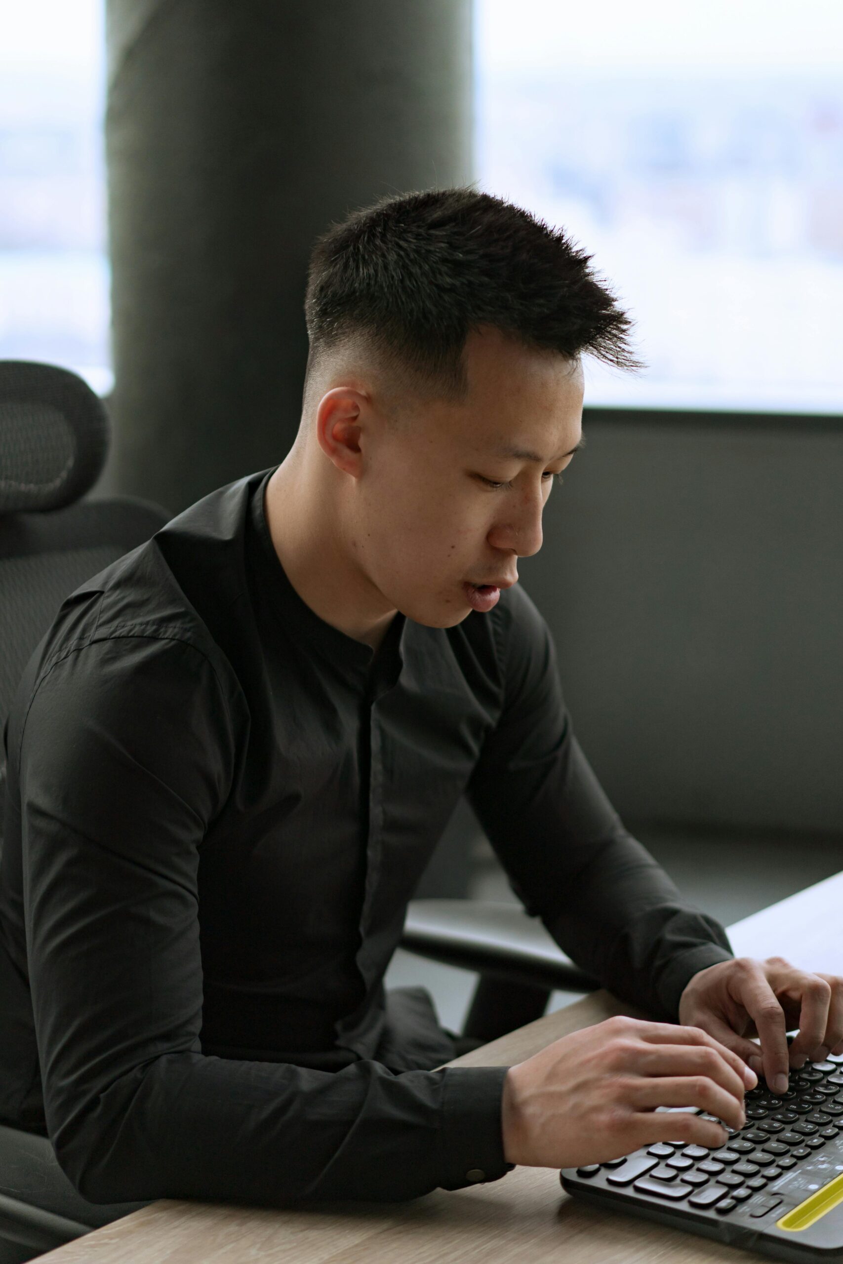 Asian man working intently on a computer keyboard in an office setting.